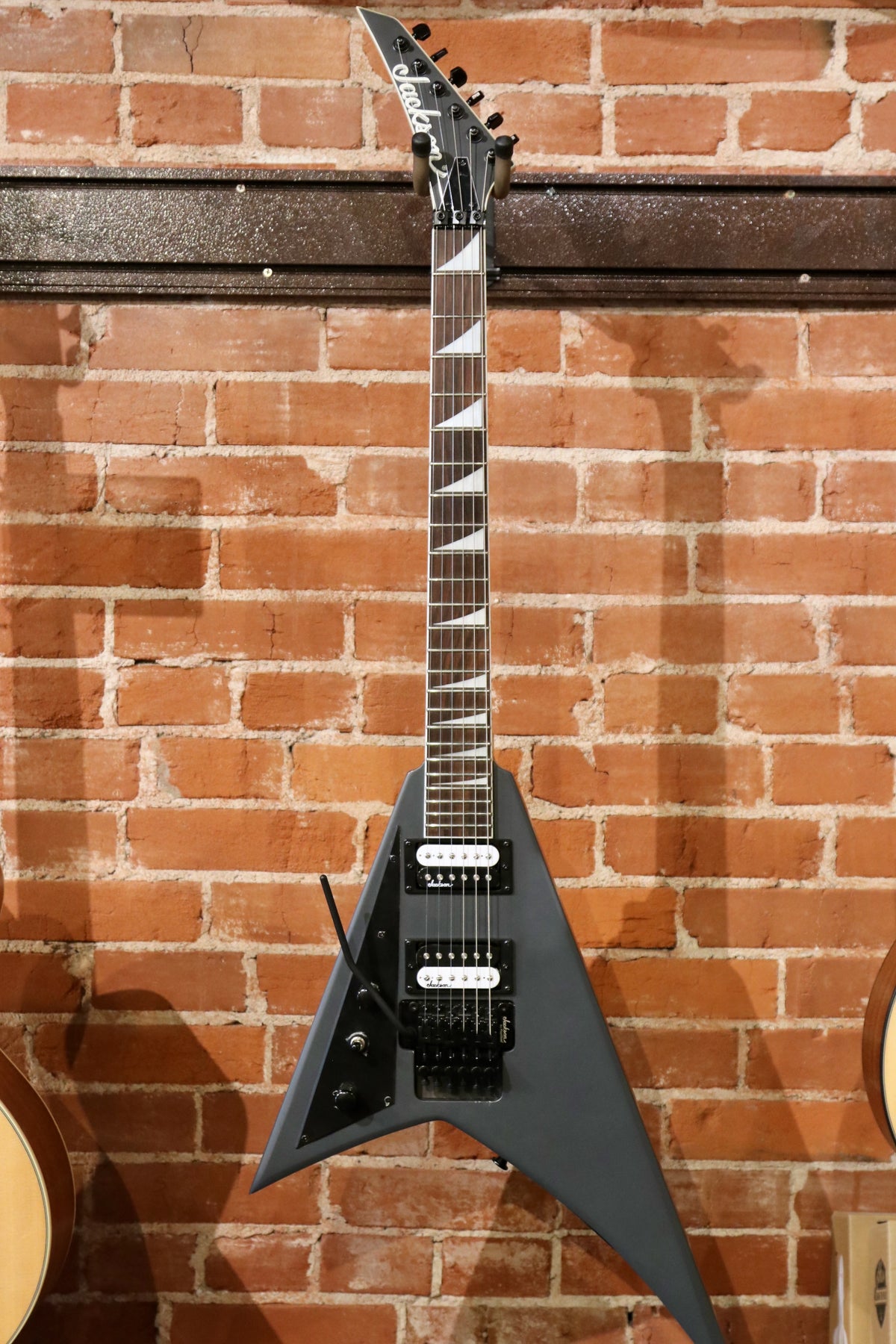 Jackson electric guitar left handed in matte black finish, front view against brick wall