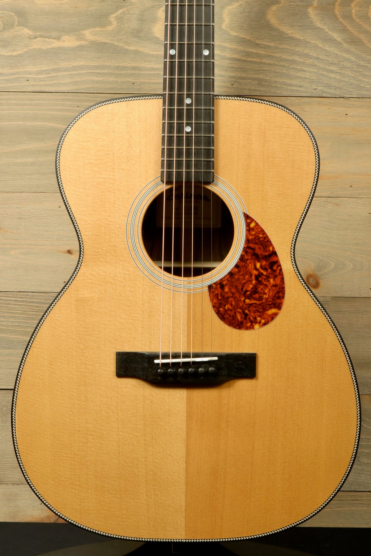 Close-up view of the top of the Eastman E3OME acoustic guitar showcasing its solid Sitka spruce top with a tortoise shell pickguard and ebony bridge, with detailed fretboard and neck.