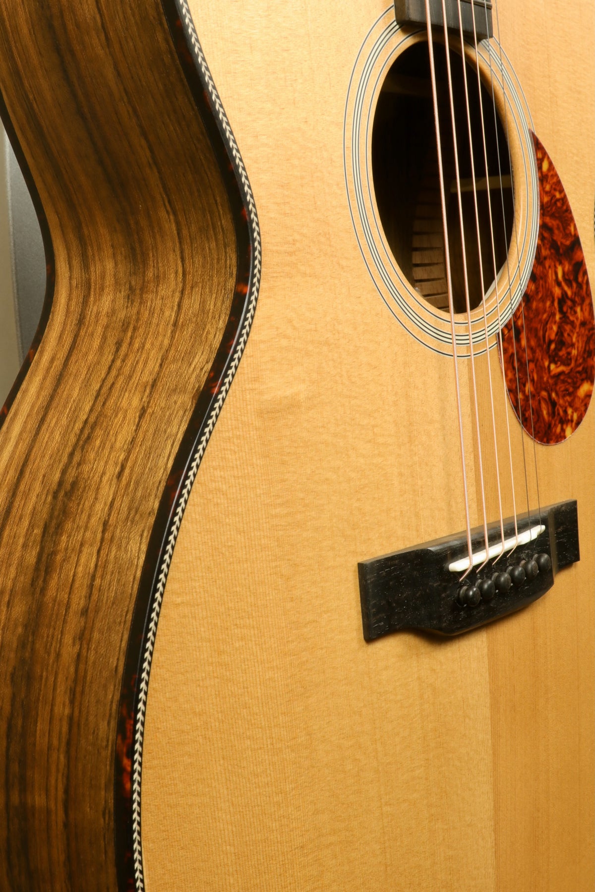 Close-up view of the body of the Eastman E3OME acoustic guitar, highlighting the stylish pickguard, ebony bridge, and silver strings.