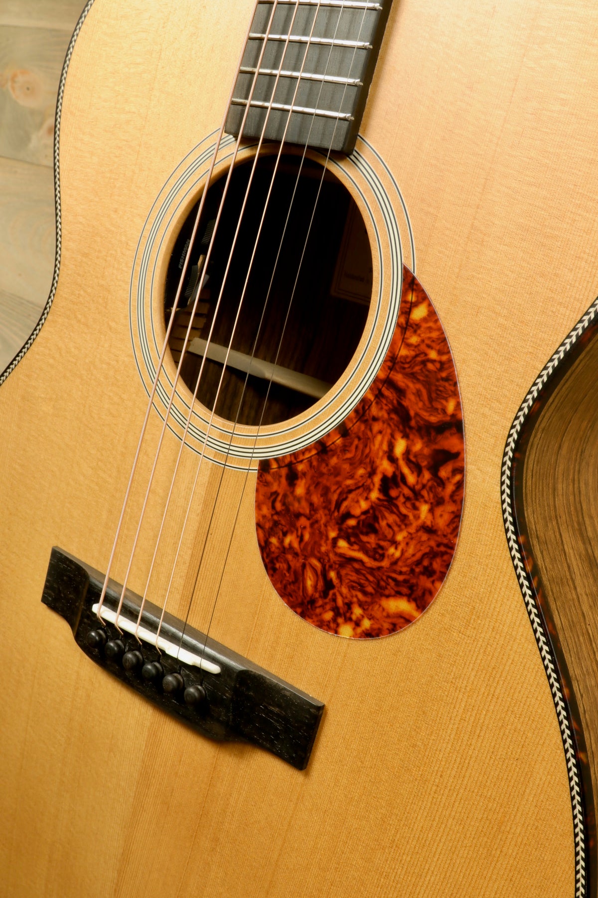 Intimate close-up of the guitar's body featuring the ebony bridge and strings, showing the detailed craft of the Eastman E3OME acoustic guitar.