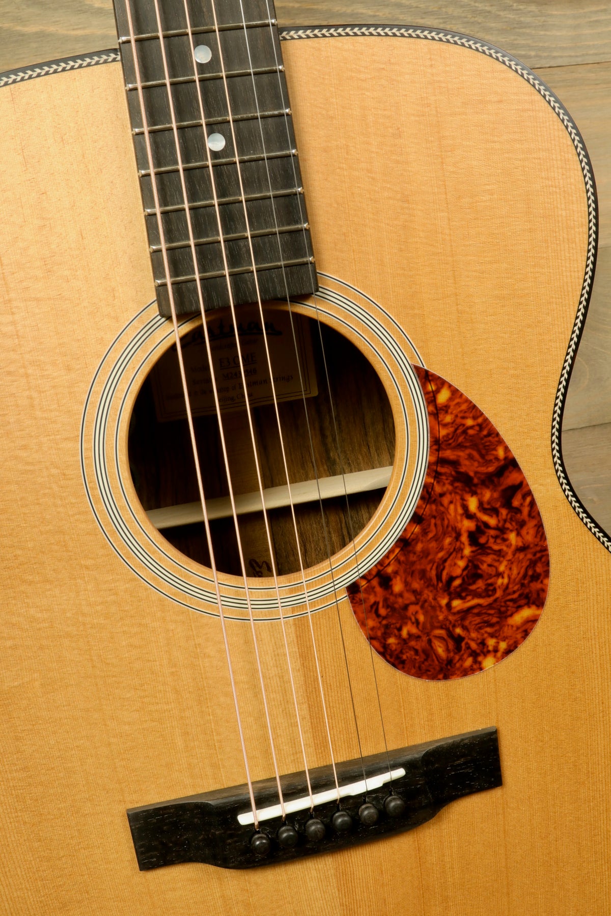 Close-up shot of the Eastman E3OME guitar's body and bridge, showcasing the intricate details of wood grain and craftsmanship.