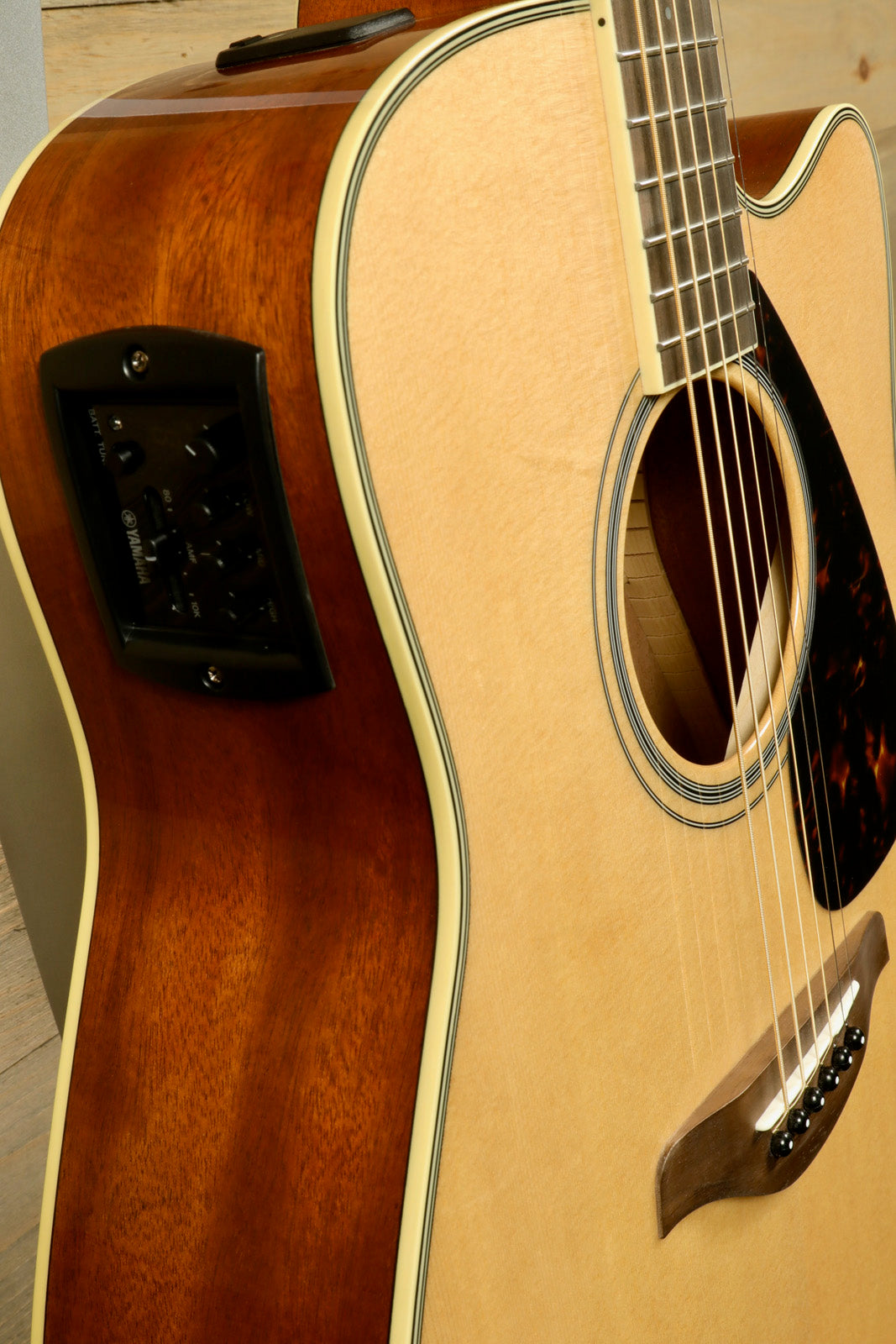 Yamaha acoustic electric guitar with natural finish and control panel, side view