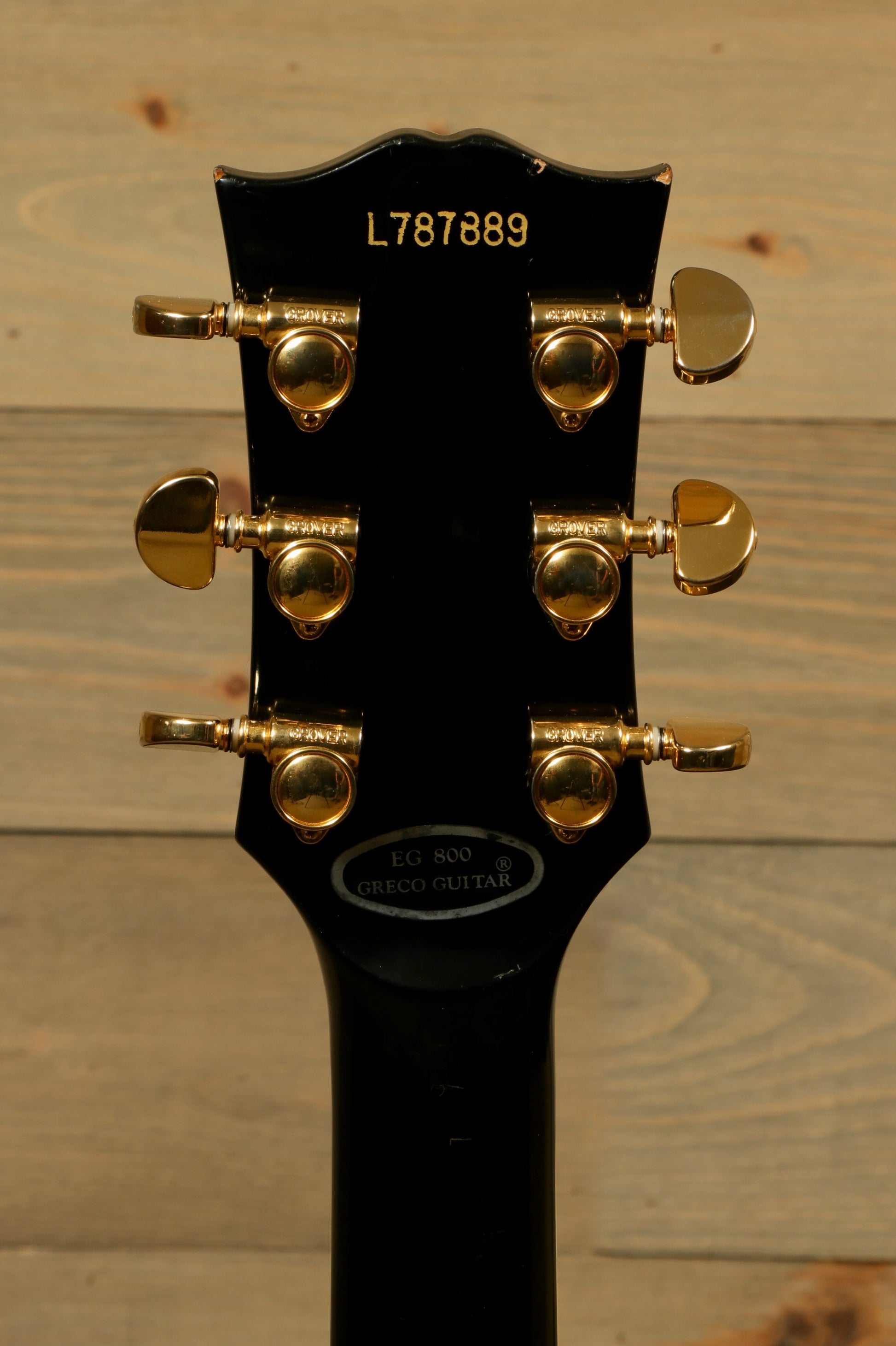 Greco guitar with a sleek black finish and gold tuning pegs, rear view of the headstock