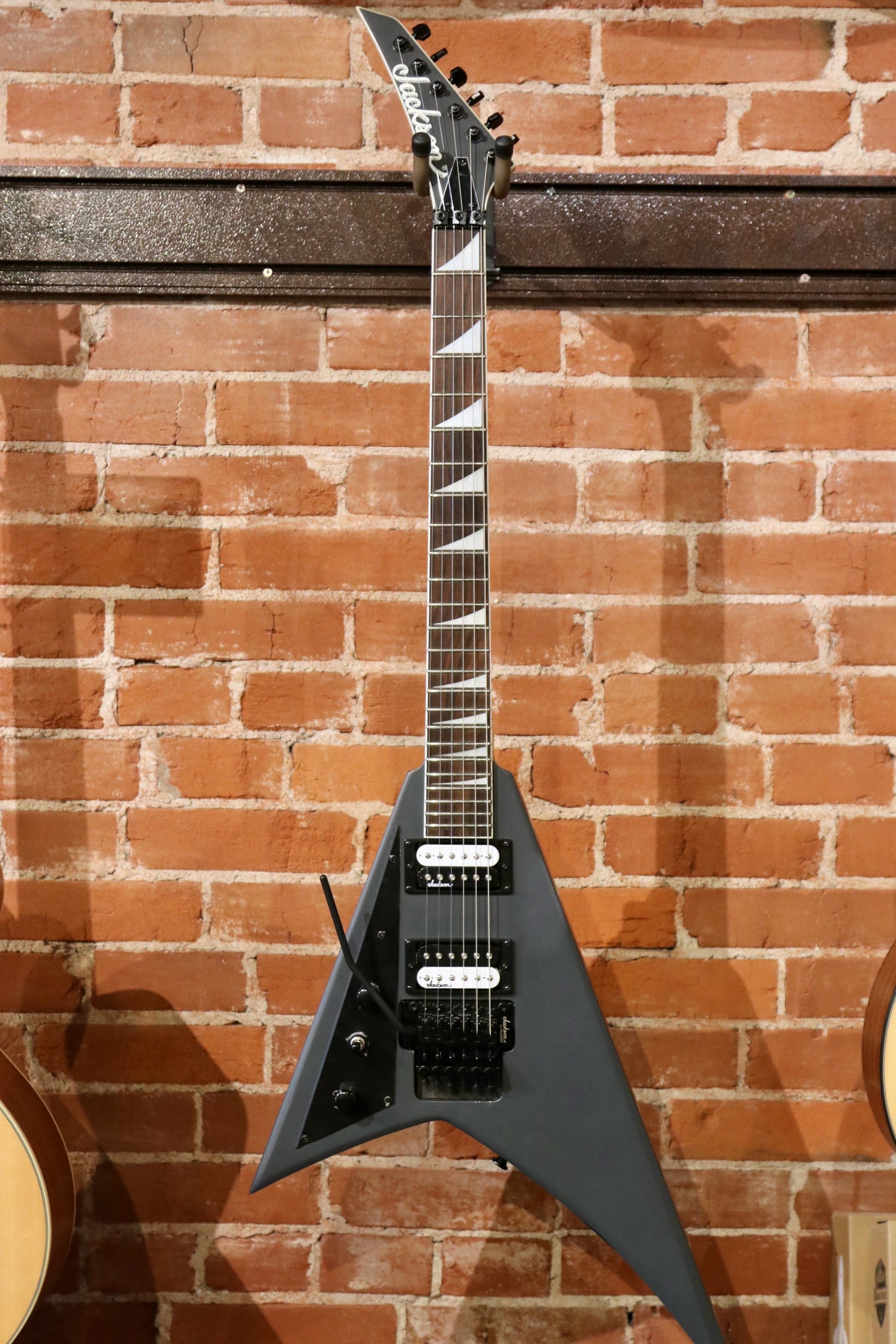 Jackson electric guitar left handed in matte black finish, front view against brick wall