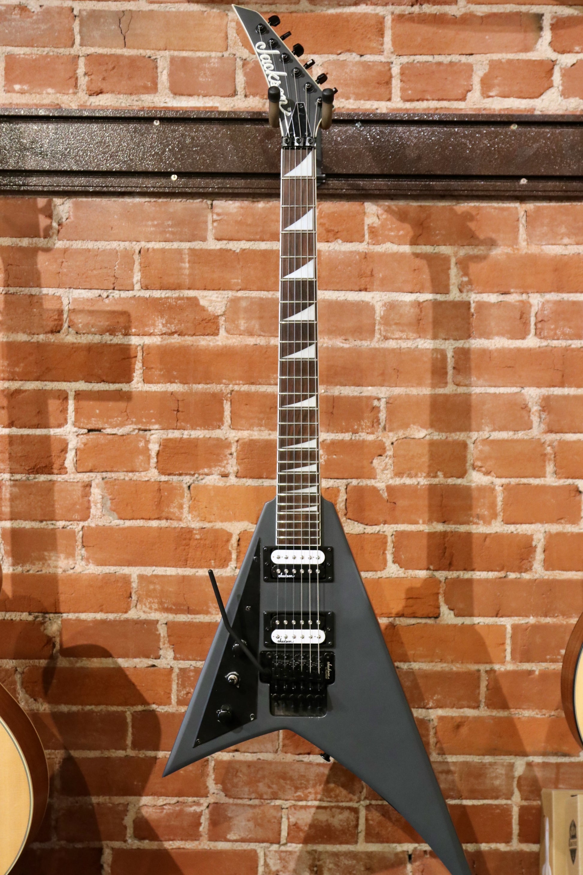 Jackson electric guitar left handed in matte black finish, front view against brick wall