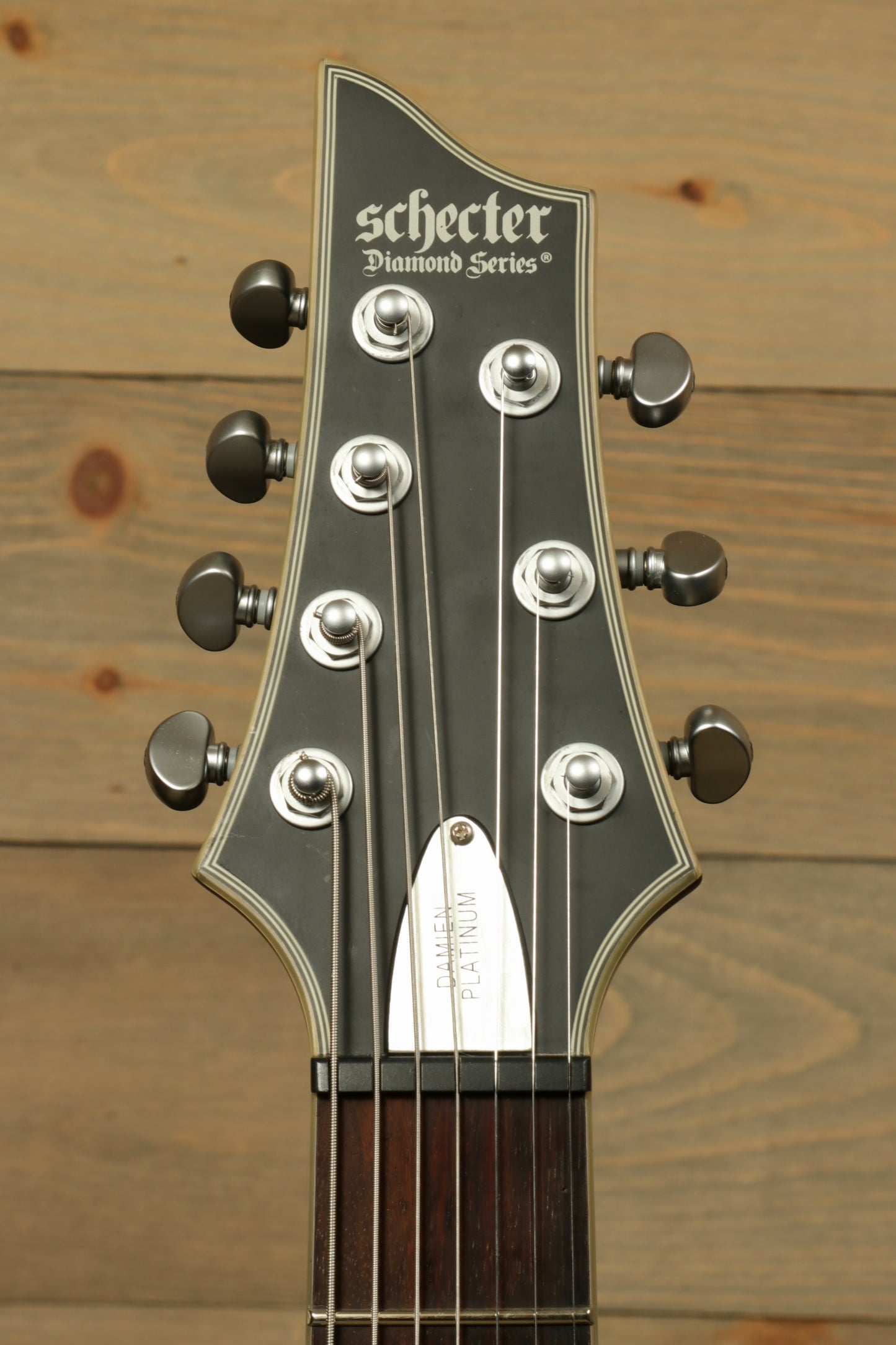 Headstock of a used Schecter Damien 7 Platinum guitar with six tuning pegs and brand logo