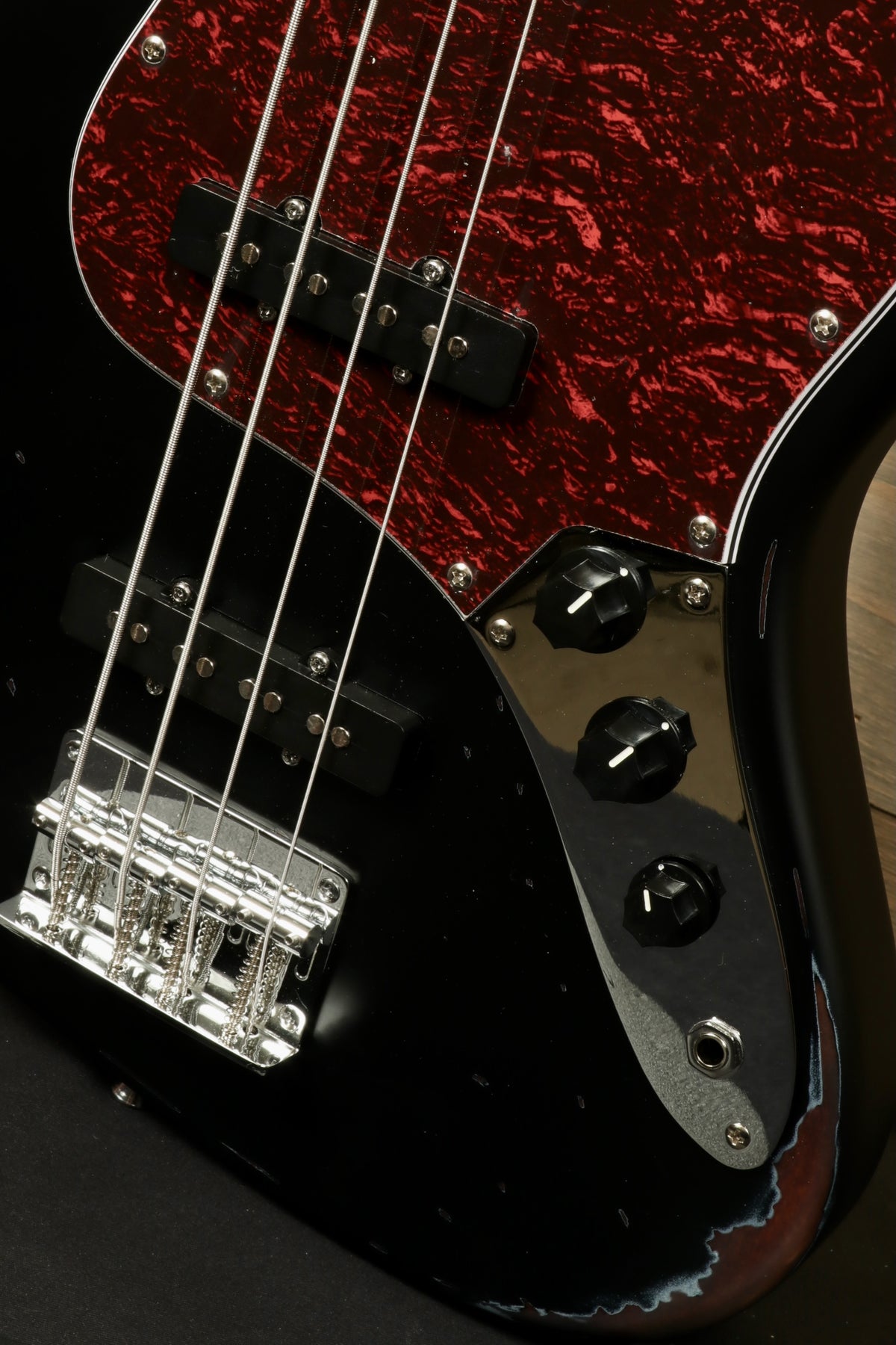 Tagima TBA-73 Electric Bass in black with red pearloid pickguard and chrome hardware, close-up view