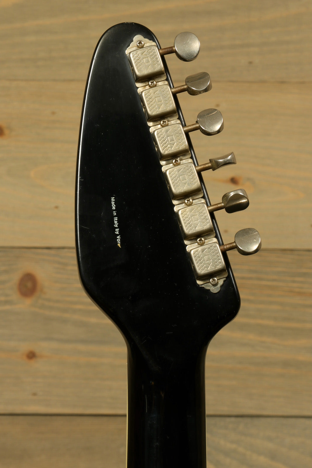 Rare Vintage Vox Guitar headstock with chrome tuning pegs, front view against rustic wood background
